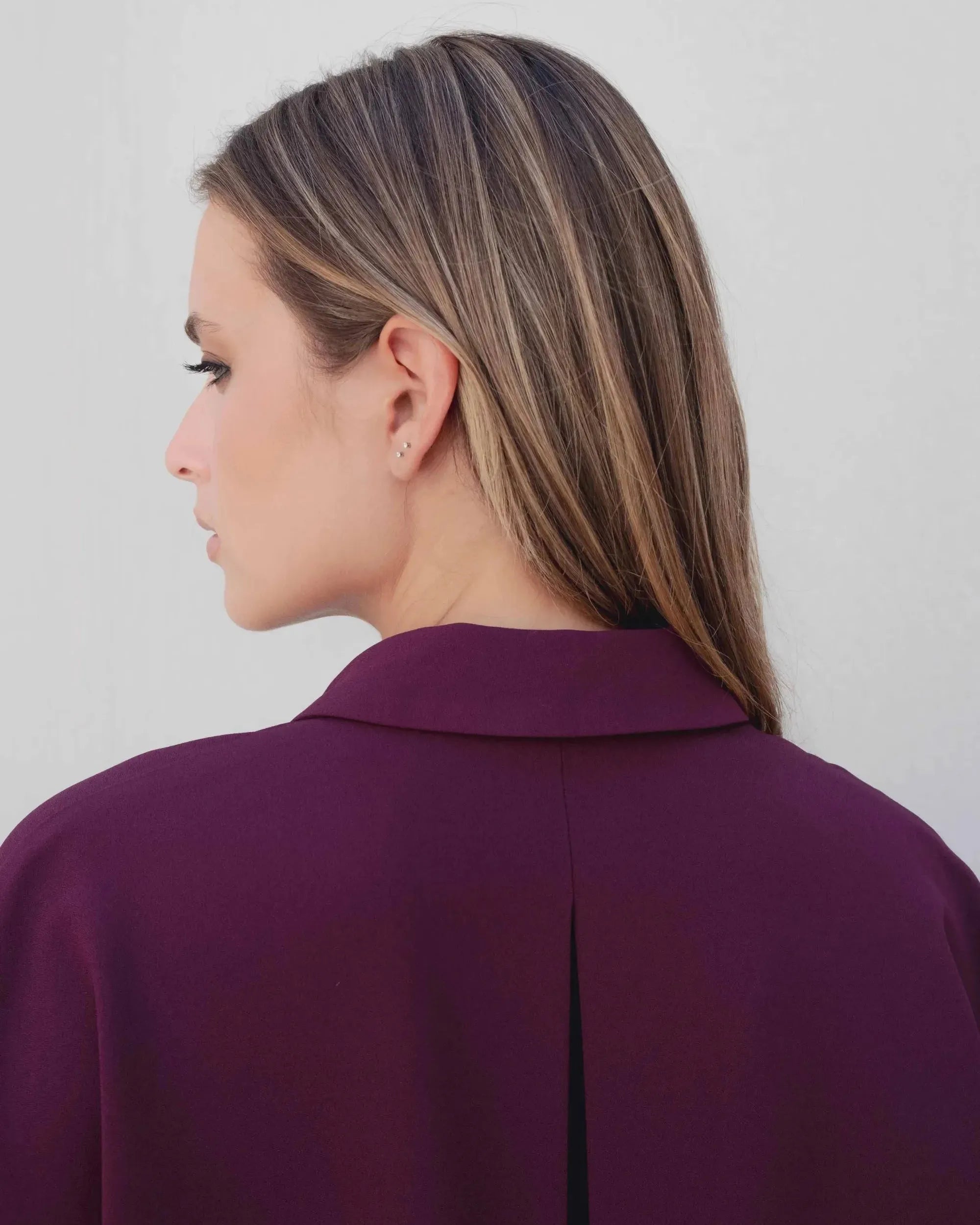 Vue arrière d'une femme portant la chemise élégante bordeaux à boutons dorés, montrant la coupe soigneusement conçue. Idéale pour ajouter une touche sophistiquée à la collection de chemises bordeaux femme.