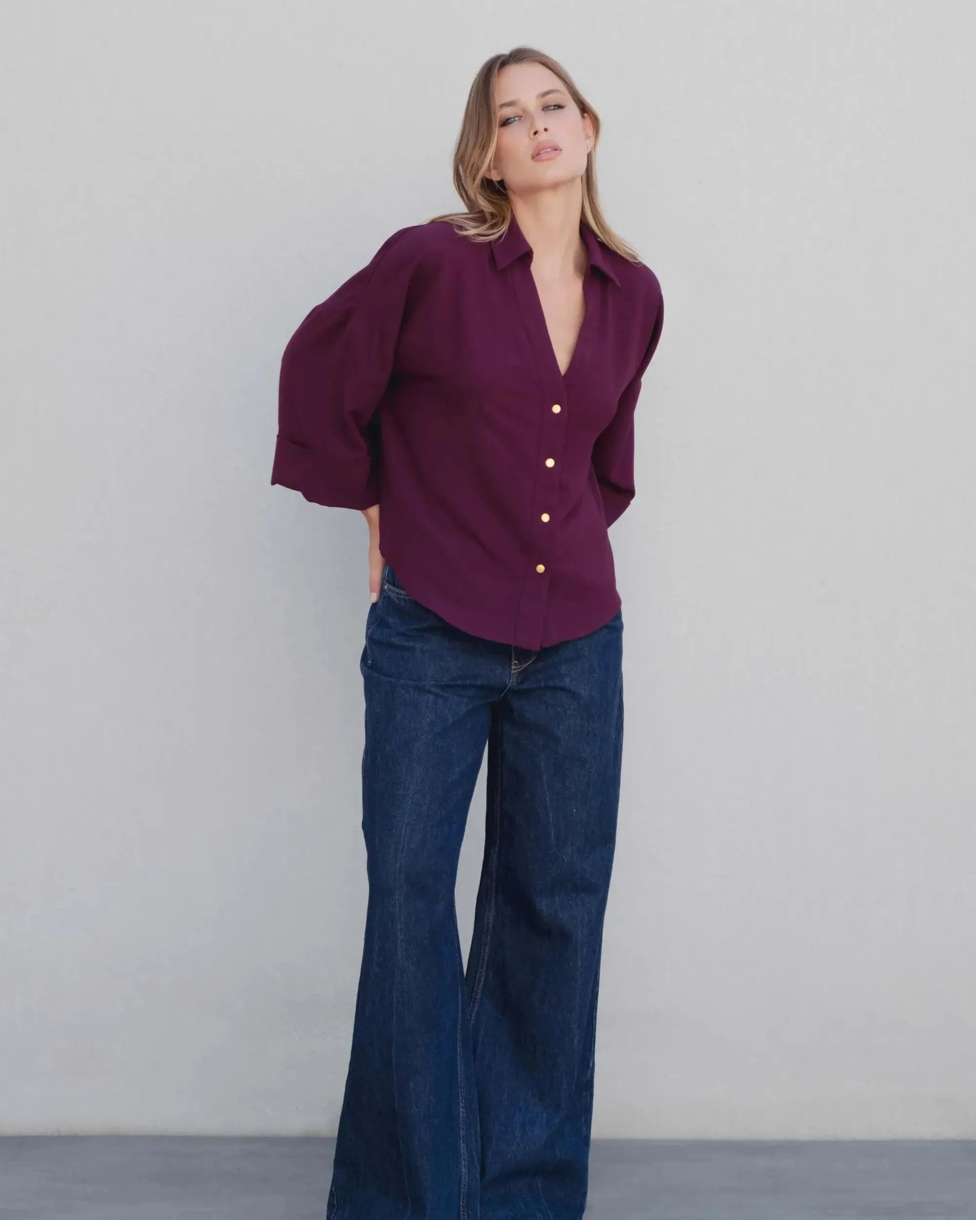 Femme portant une chemise élégante bordeaux à boutons dorés, associée à un jean large, illustrant un look casual chic. Cette chemise bordeaux femme est parfaite pour diverses occasions.