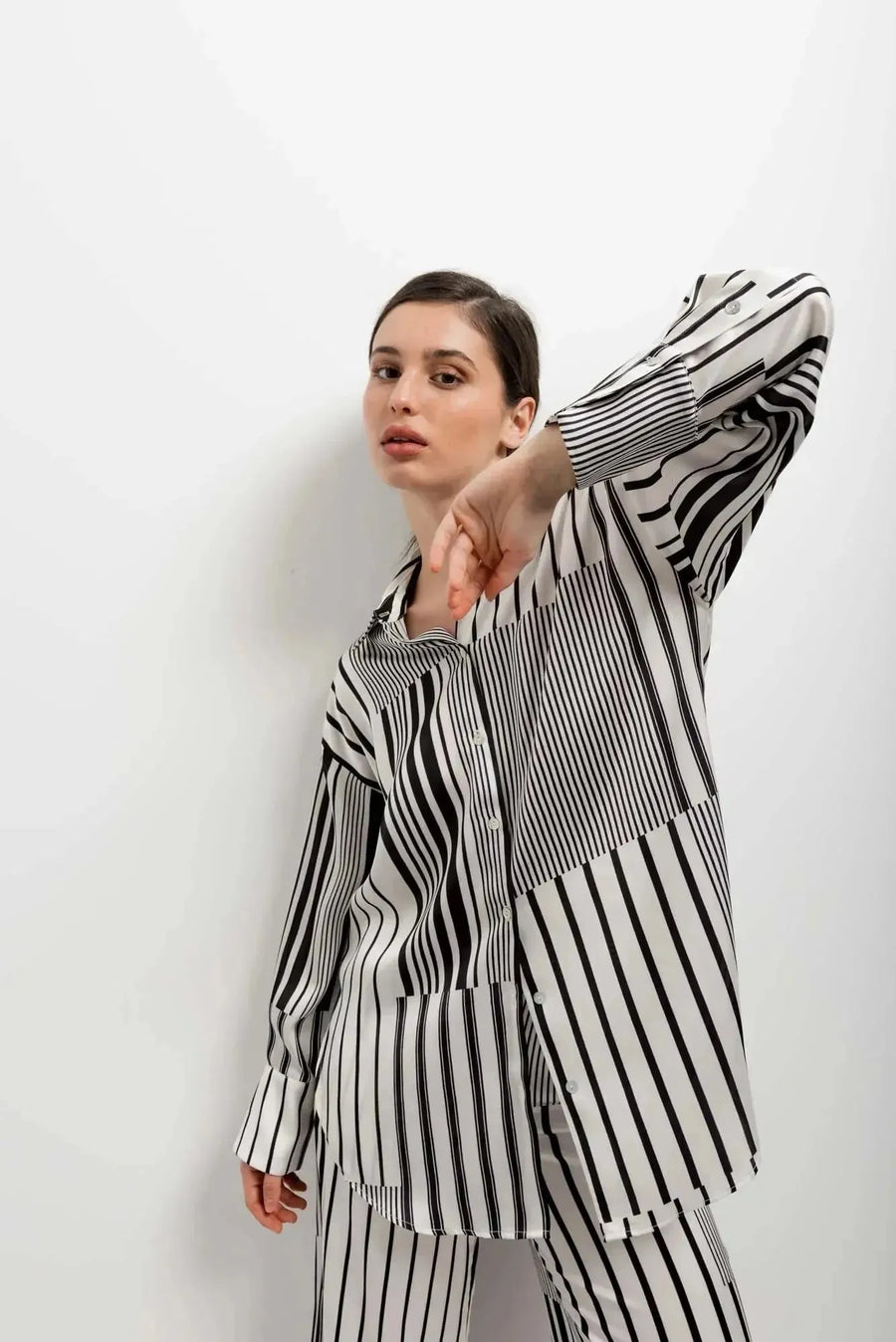 Femme posant en chemise rayée femme ajustée à manches longues, combinée avec un fond minimaliste, illustrant un style moderne.