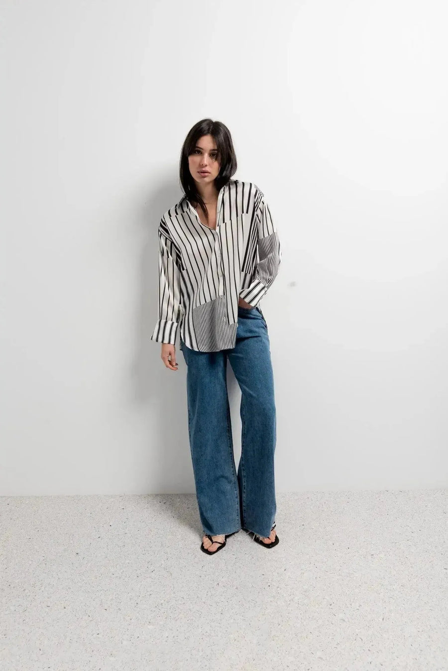 Modèle dans une chemise rayée femme ajustée à manches longues, accompagnée de jeans amples, offrant un look casual-chic parfait.