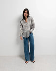 Modèle dans une chemise rayée femme ajustée à manches longues, accompagnée de jeans amples, offrant un look casual-chic parfait.