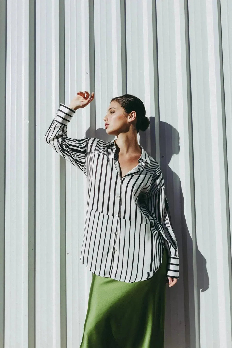 Modèle portant une chemise rayée femme ajustée à manches longues, affichant un look élégant et confortable devant un mur métallique.