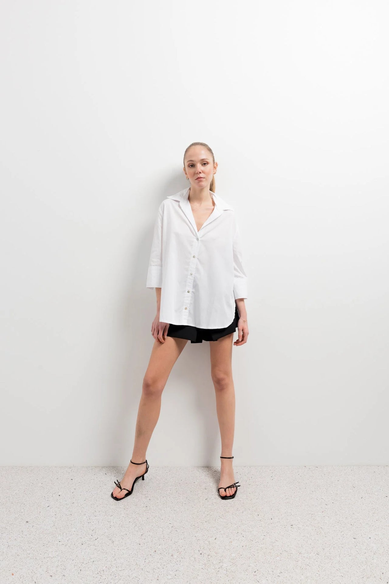 Chemise Femme Blanche Ample en popeline, modèle se tenant debout avec une attitude confiante dans un studio moderne.