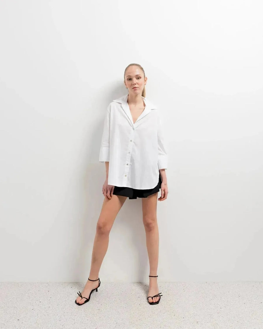 Chemise Femme Blanche Ample en popeline, modèle se tenant debout avec une attitude confiante dans un studio moderne.