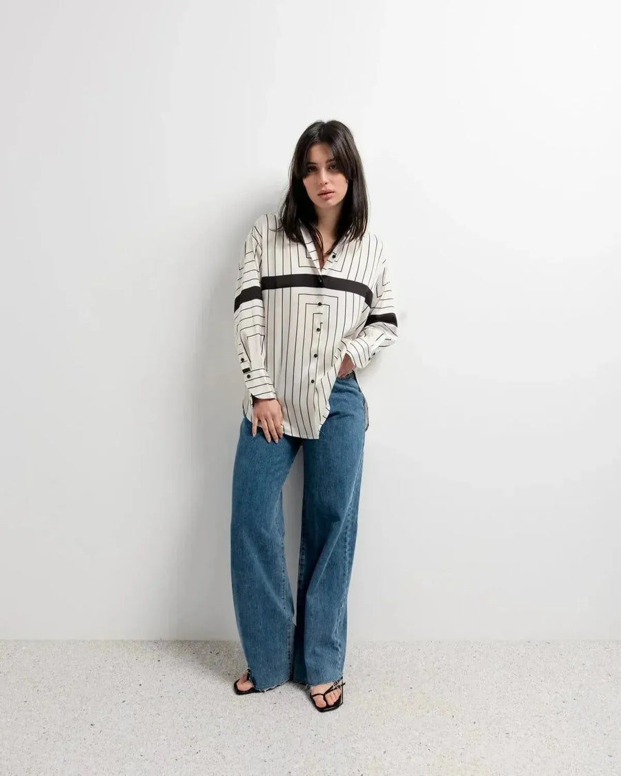 Chemise Femme Imprimée à Rayures Noires portée par une jeune femme, illustrant un look moderne avec sa coupe ample fluide associée à un jean.