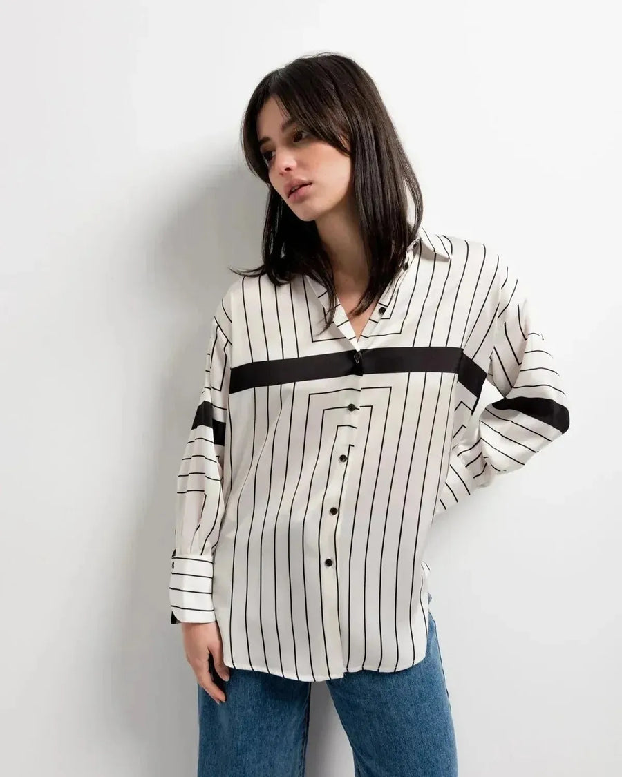 Chemise Femme Imprimée à Rayures Noires présentée par une femme devant un fond minimaliste, mettant en avant son style ample fluide pour toutes les occasions.