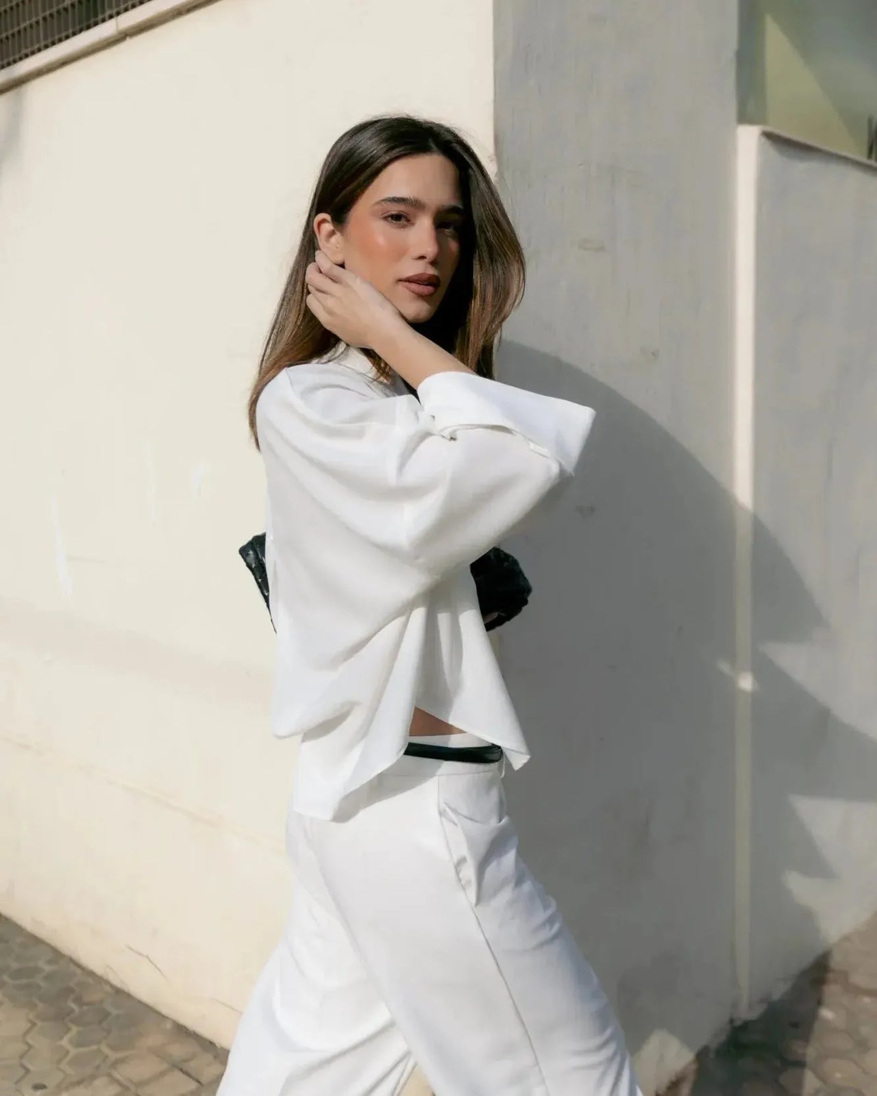 Une femme se promenant dans la rue en portant une chemise fluide blanche à manches larges et dos fendu, accentuant la simplicité et le style décontracté de ce chemisier ample femme.