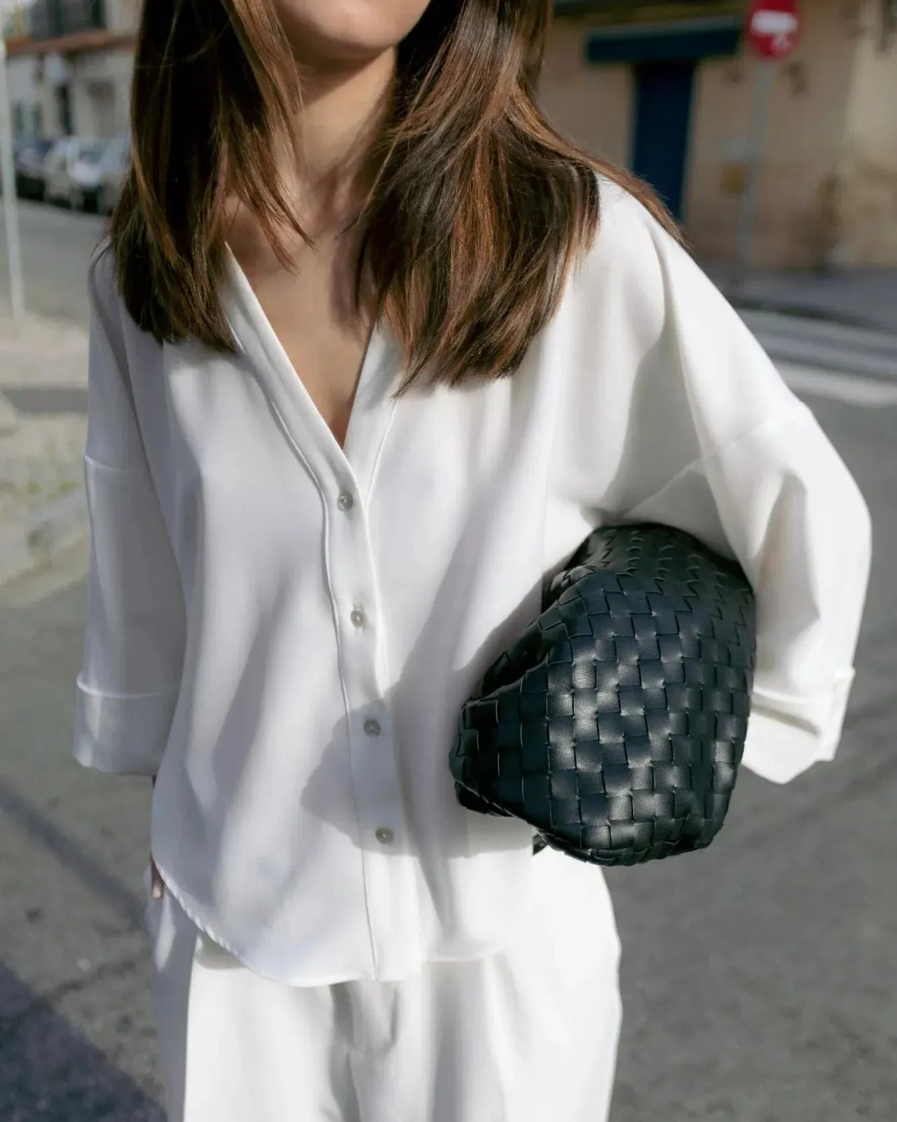 Une femme en tenue chic avec une chemise fluide blanche à manches larges et dos fendu, tenant un sac noir, illustrant la polyvalence de ce chemisier ample femme.