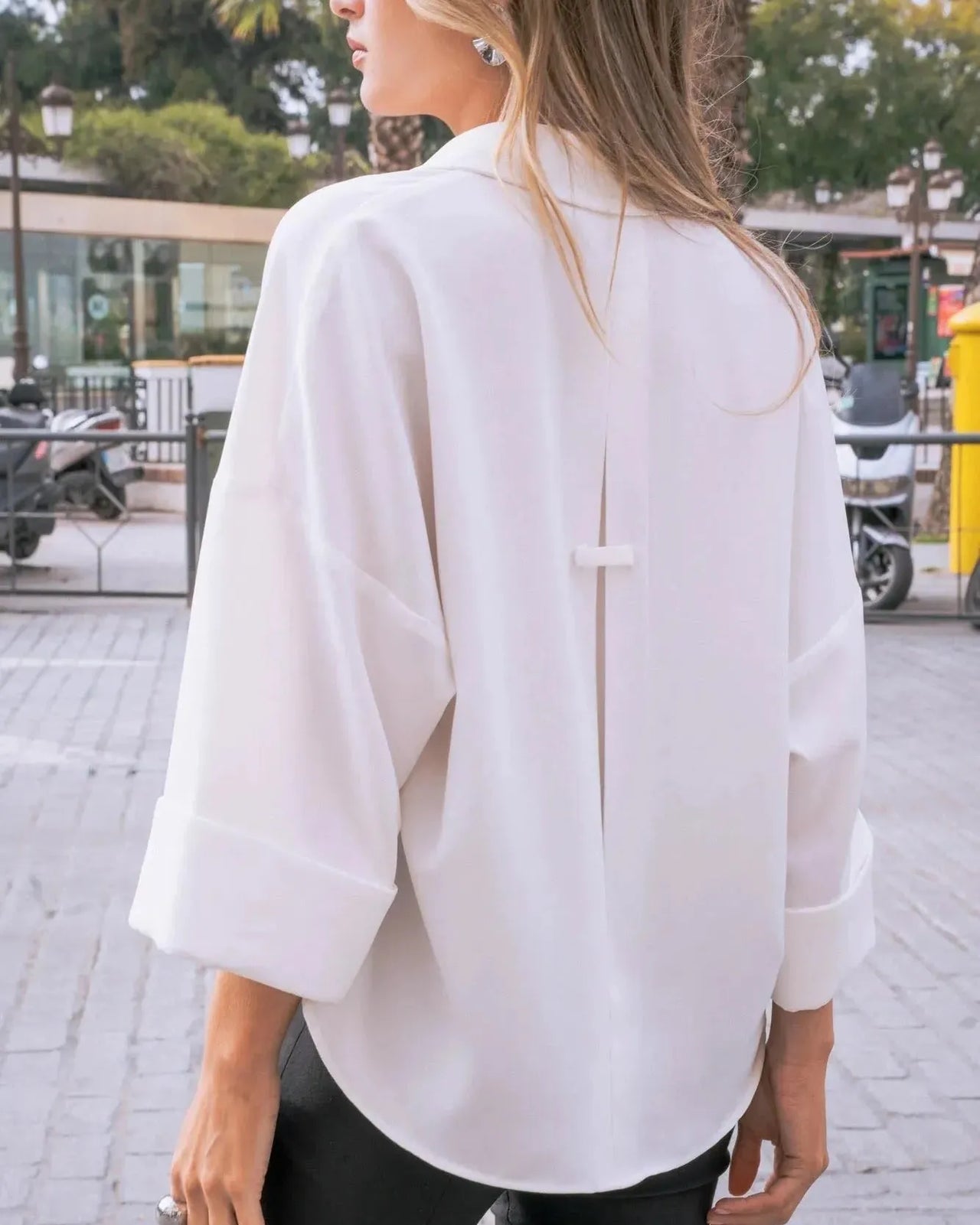 Vue de derrière d'une femme portant une chemise fluide blanche à manches larges et dos fendu, mettant en valeur le design moderne de ce chemisier ample femme.