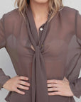 Femme portant une chemise col lavallière fluide marron transparent, mettant en avant le col lavallière noué et les détails de la chemise col lavallière.