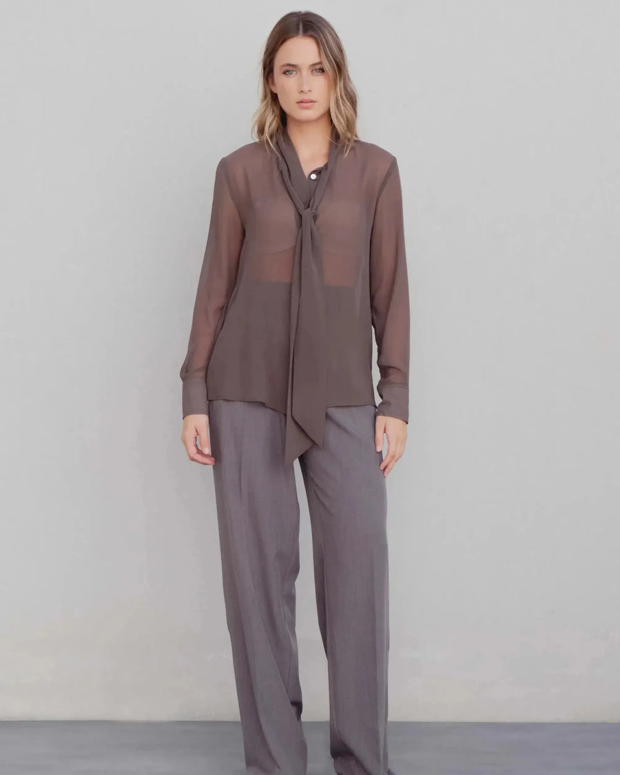Femme habillée avec une chemise col lavallière fluide marron transparent, associée à un pantalon élégant, parfaite pour un look moderne.