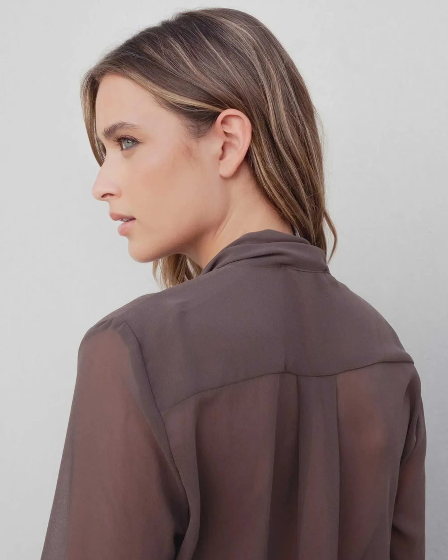 Vue latérale d'une femme portant une chemise col lavallière fluide marron transparent, montrant le col et la coupe sophistiquée de la chemise col lavallière.