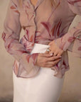 Femme ajustant sa chemise fleurie femme semi-transparente, dévoilant son style raffiné et chic.