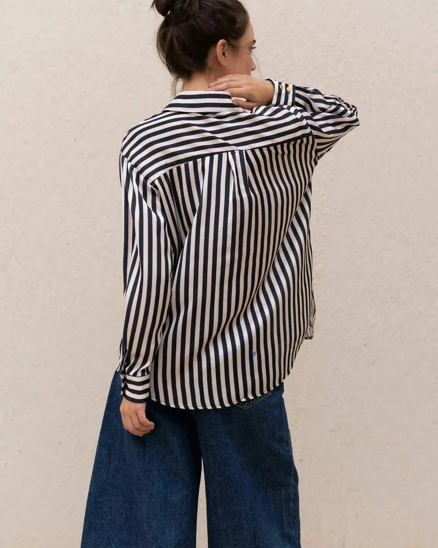 Vue arrière d'une femme portant une chemise rayée bleu marine et blanc, associée à un jean ample, illustrant un style décontracté et élégant, parfait avec la chemise rayée femme.
