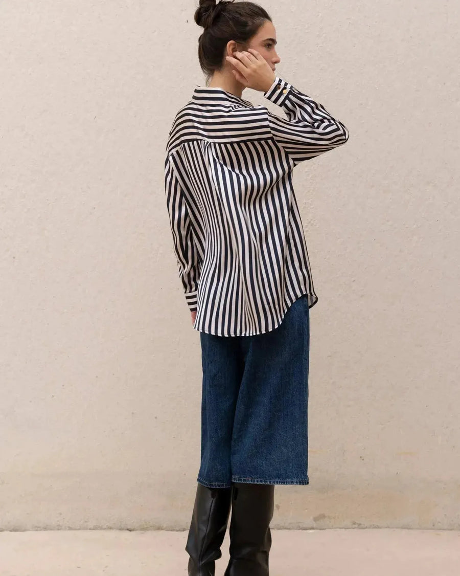 Femme de dos en chemise rayée bleu marine et blanc, ajustée à un jean, montrant un look contemporain et à la mode, complément idéal pour la chemise rayée femme.