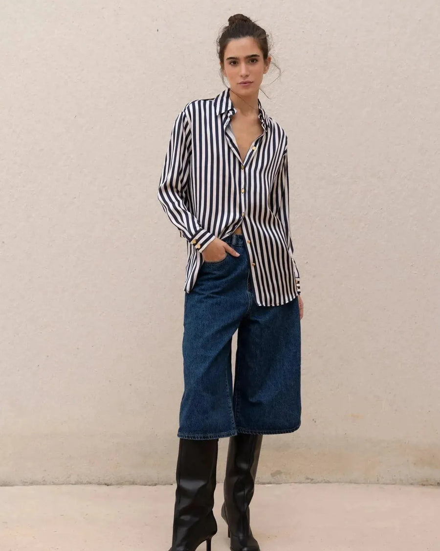 Modèle portant une chemise rayée bleu marine et blanc pour femme avec un look décontracté, associée à un jean ample et des bottes noires. Idéale pour un style contemporain avec la chemise rayée femme.