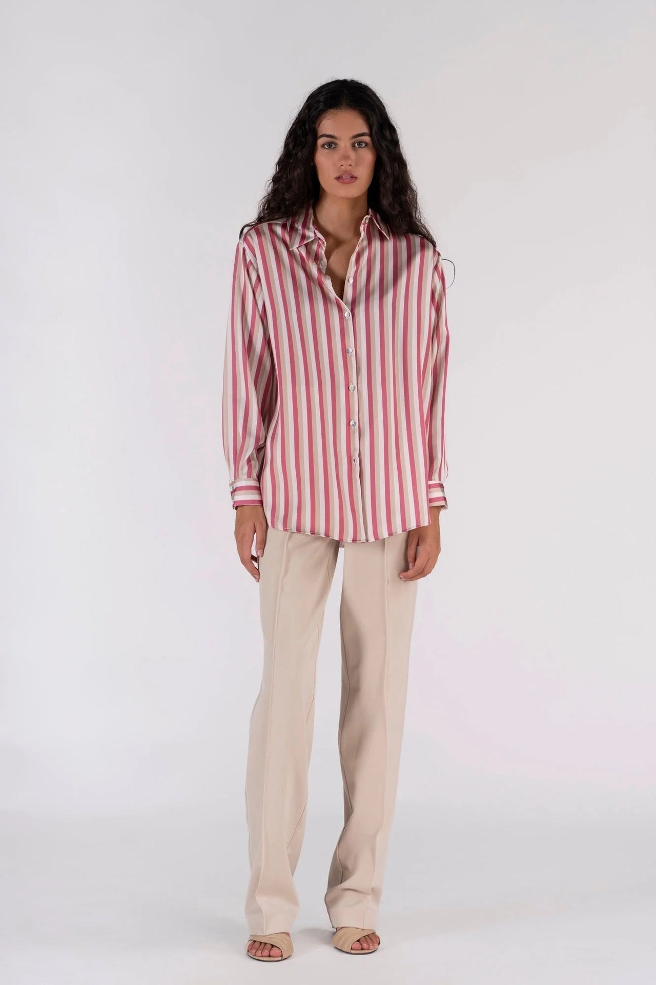 Chemisier satin femme chic à rayures verticales, couleur rose et beige, porté avec un pantalon beige pour un look sophistiqué, mannequin élégant en studio.