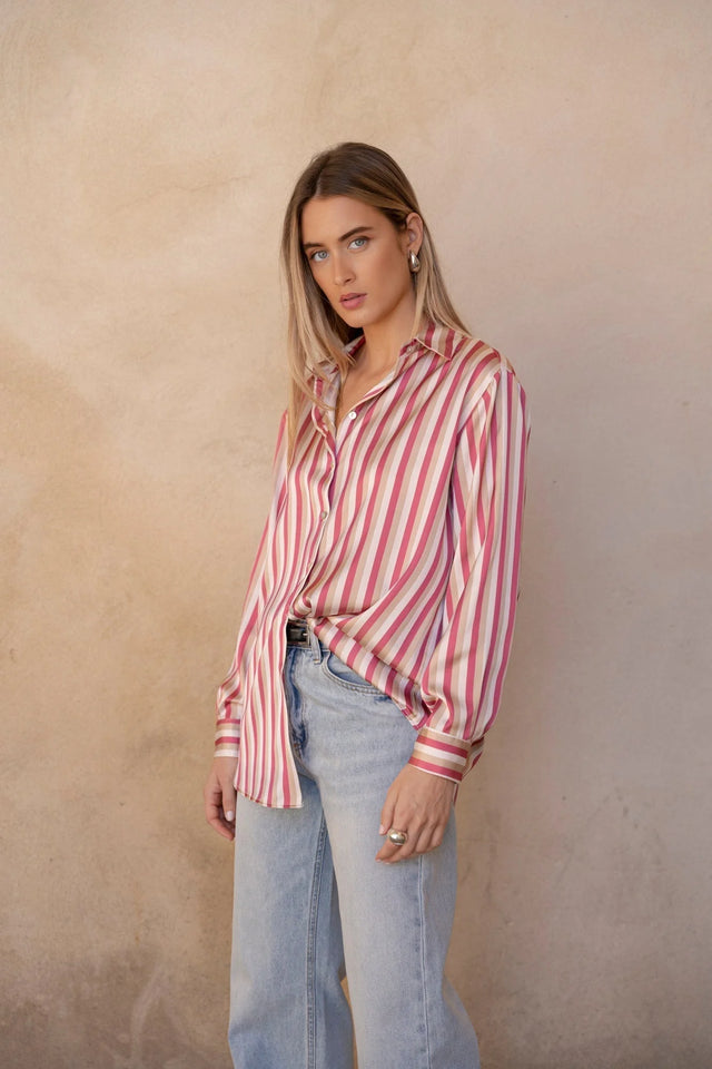 Chemisier satin femme chic à rayures verticales, couleur rose et beige, porté avec un look tendance, modèle élégant dans un décor neutre.