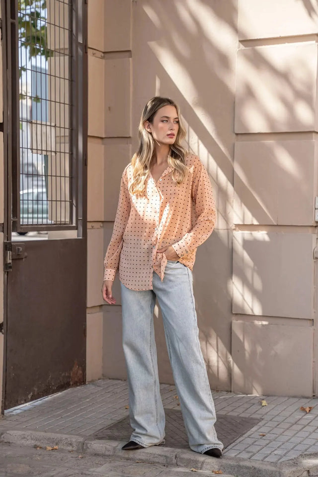 Chemise Transparente Femme À Pois Noirs présentée dans un cadre urbain, combinée à un jean, offrant une allure moderne et stylée.