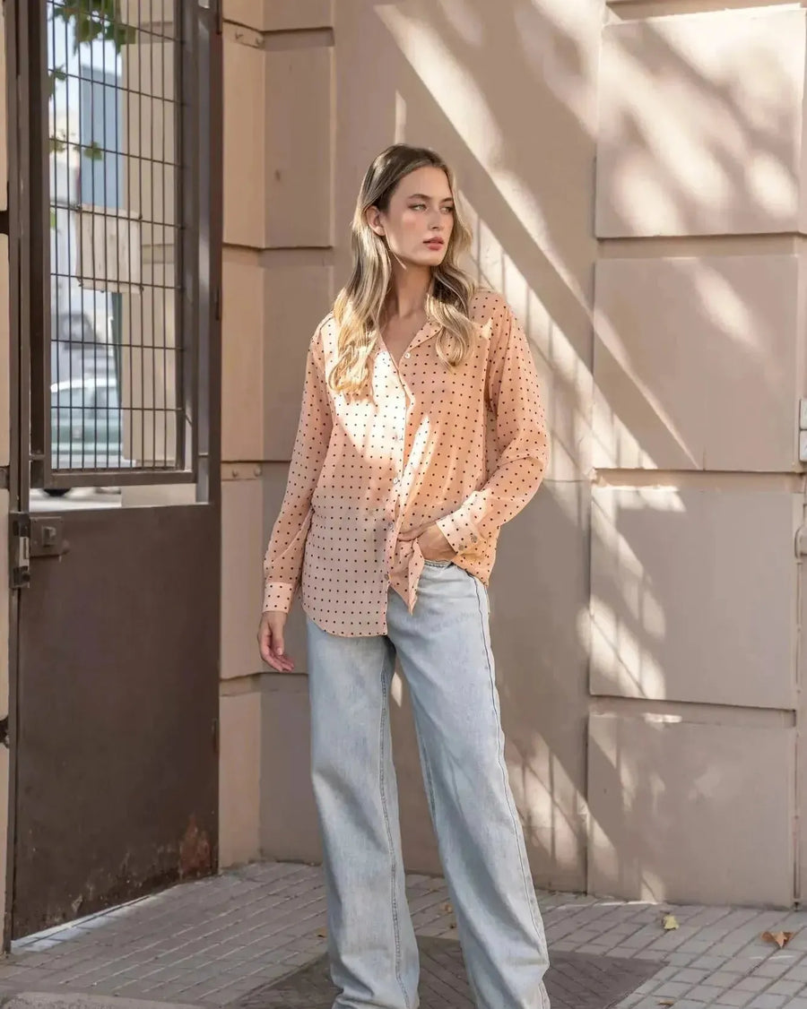 Chemise Transparente Femme À Pois Noirs présentée dans un cadre urbain, combinée à un jean, offrant une allure moderne et stylée.