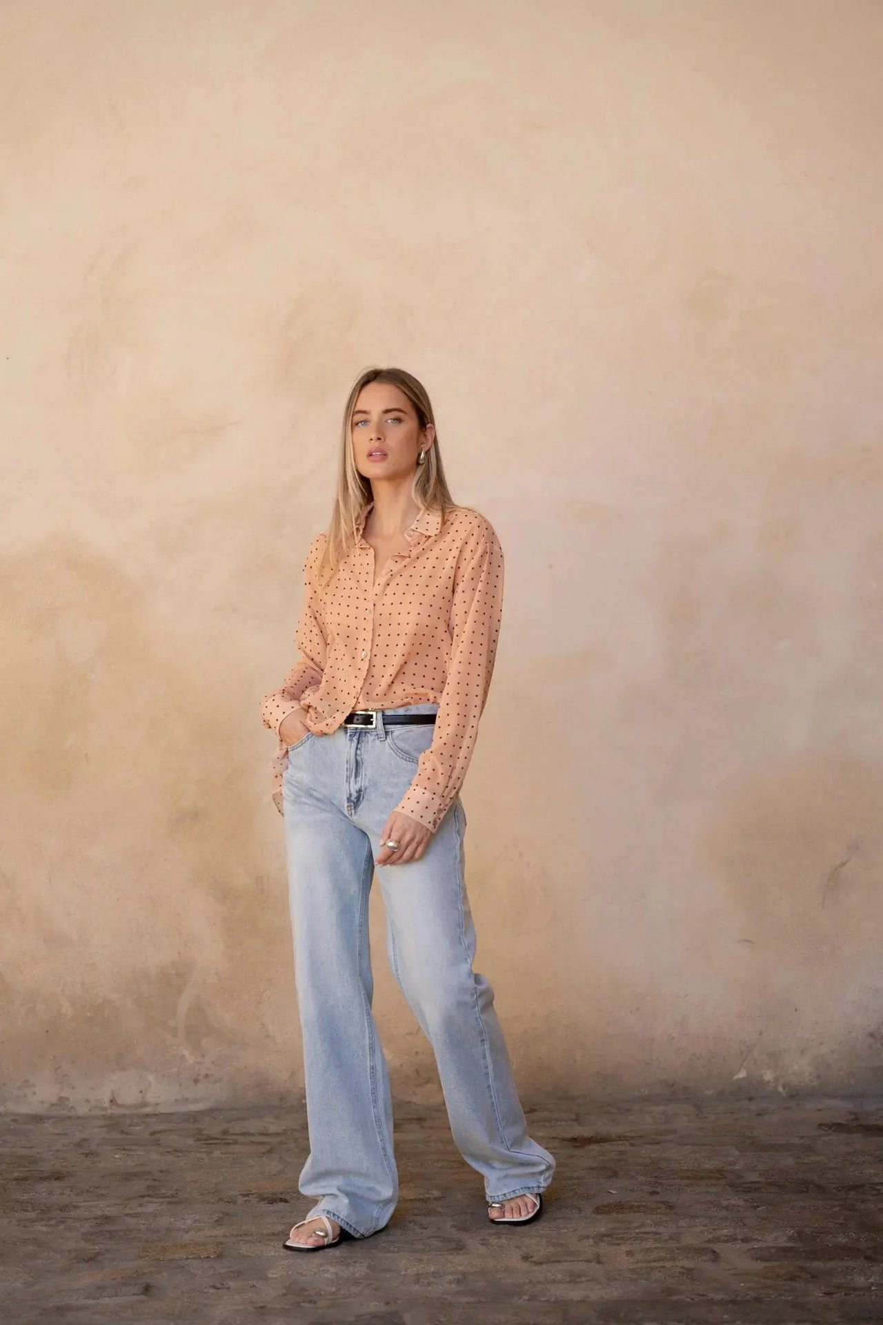 Chemise Transparente Femme À Pois Noirs – Blouse chic photographiée à l'intérieur, portée avec un jean pour un look décontracté.