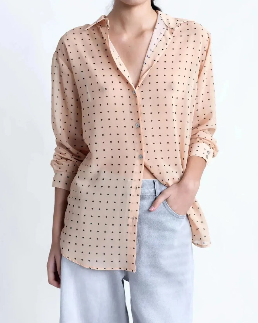 Chemise Transparente Femme À Pois Noirs – Blouse Fluide Chic Et Légère En Voile Nude portée avec un pantalon clair, mettant en valeur le motif à pois noirs sur fond nude.