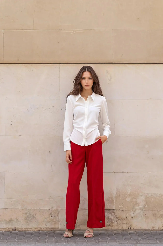 Une femme posant dans une chemise élégante à plis et un pantalon rouge, une combinaison parfaite pour toutes occasions.