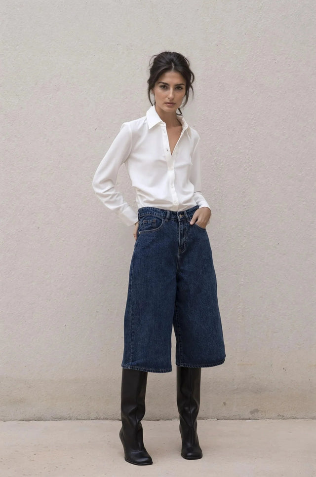 Une femme debout affichant une chemise élégante à plis, associée à un jean large pour un look chic et décontracté.