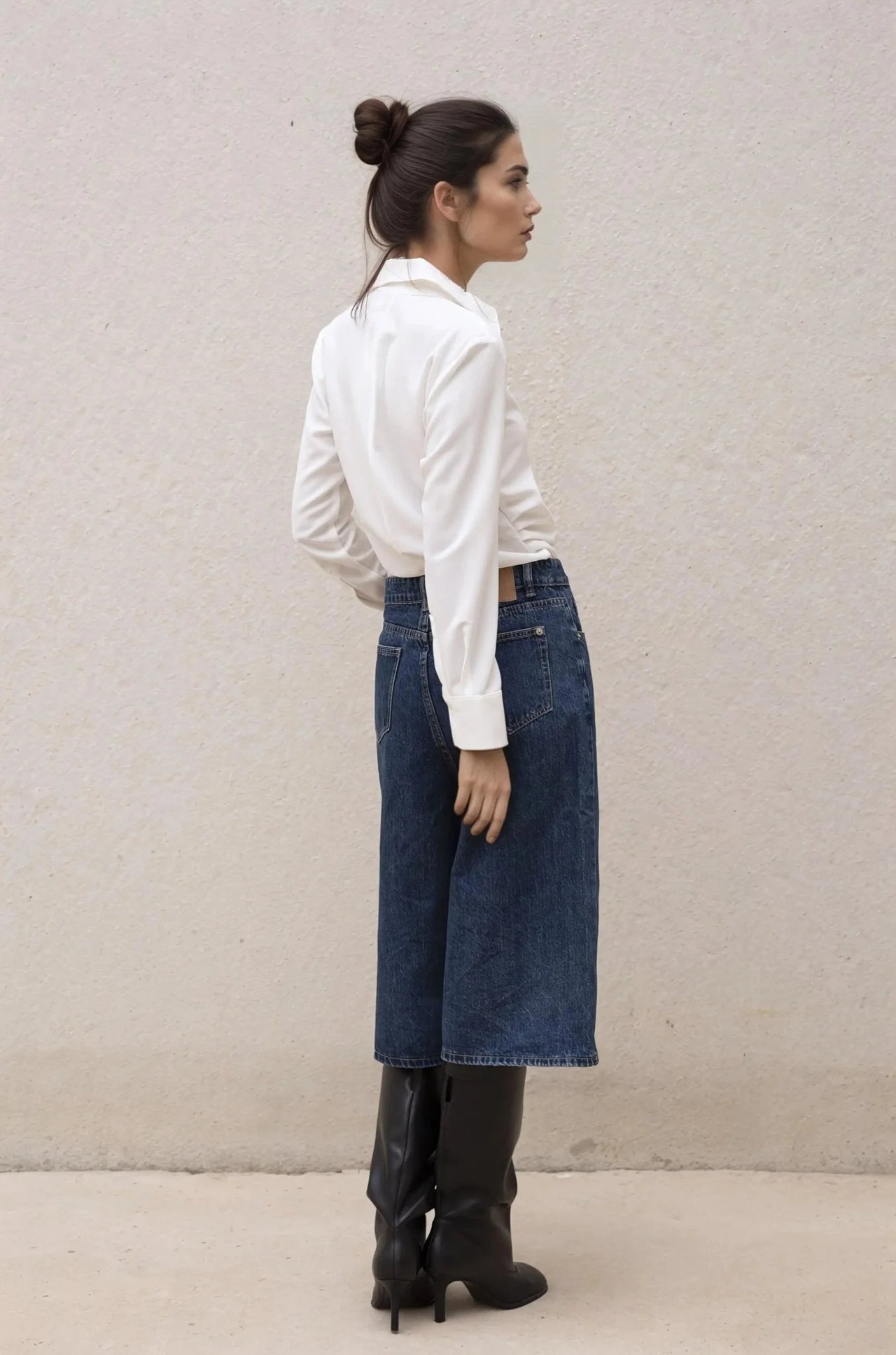 Vue arrière d'une femme avec une chemise élégante à plis, mettant en valeur le style versatile, assise avec un jean.