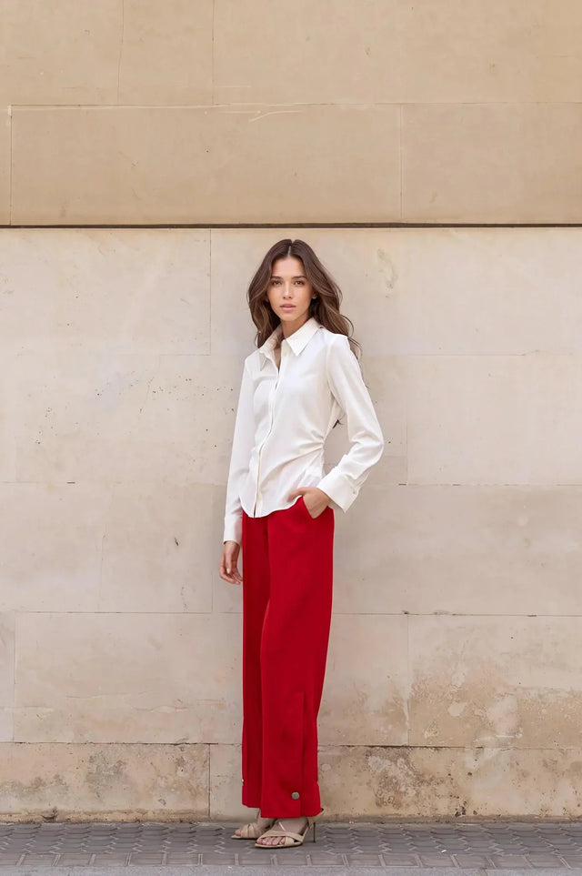 Une femme stylée en chemise élégante à plis, associée à un pantalon rouge pour un look moderne et sophistiqué.