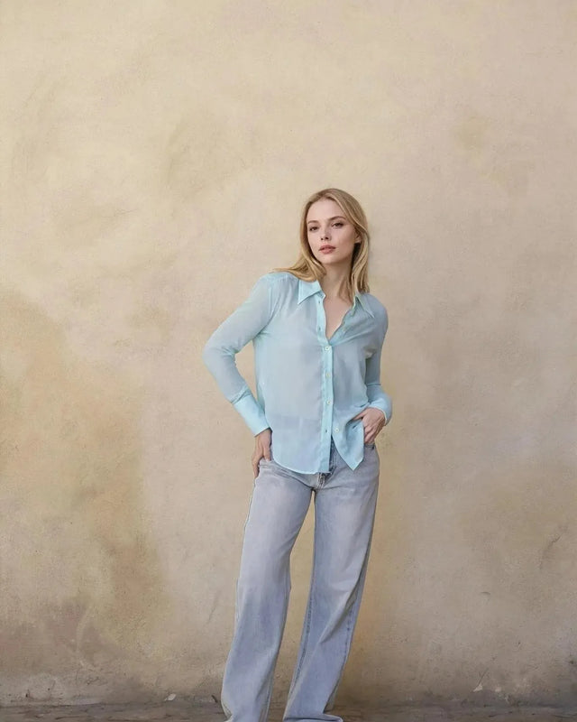 Femme élégante en chemise transparente pour femme aux accents bleus, stylisée avec un pantalon décontracté.