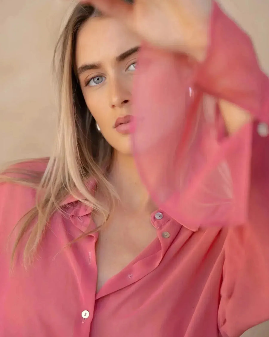 Gros plan sur une femme en chemise transparente rose à manches longues pour femme, mettant en valeur les détails du tissu léger. Un choix parfait pour toute femme à la recherche d'une chemise transparente femme.