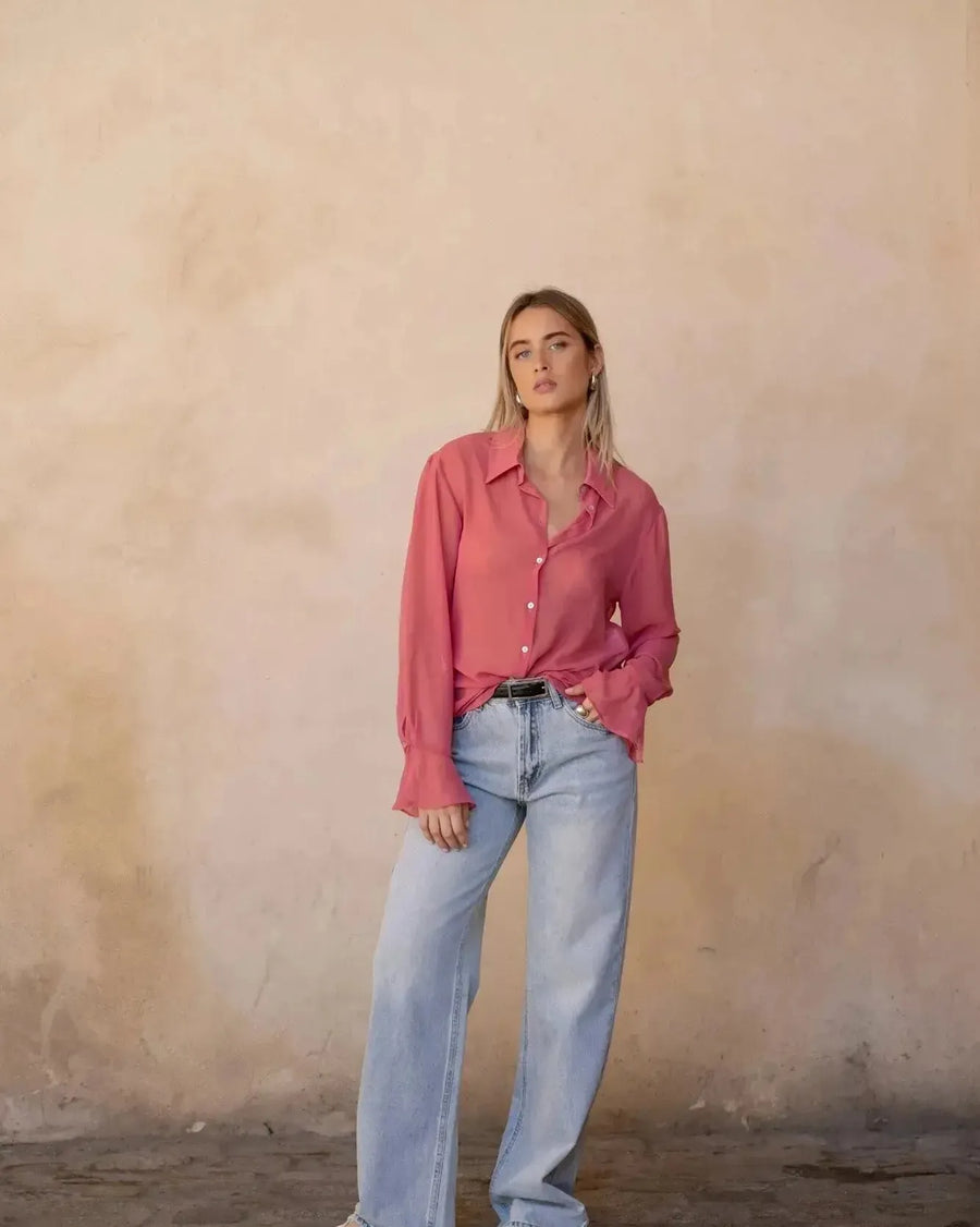 Femme stylée en chemise transparente rose à manches longues pour femme, devant un fond neutre, idéale pour un look décontracté mais chic avec la chemise transparente femme.