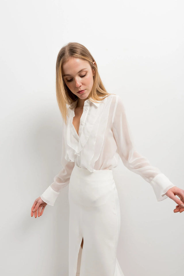 Femme portant une chemise à volants élégante en blanc, chic et polyvalente, avec un design délicat, parfaite pour diverses occasions.