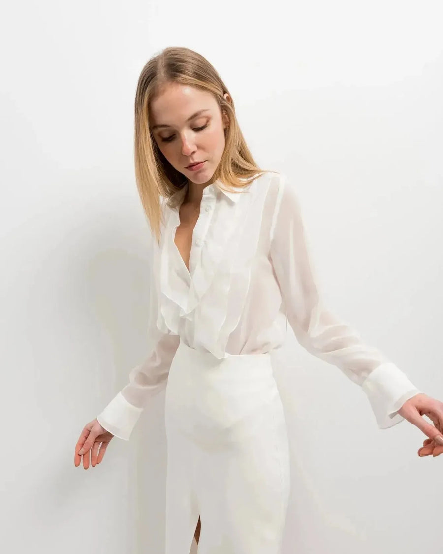 Femme portant une chemise à volants élégante en blanc, chic et polyvalente, avec un design délicat, parfaite pour diverses occasions.