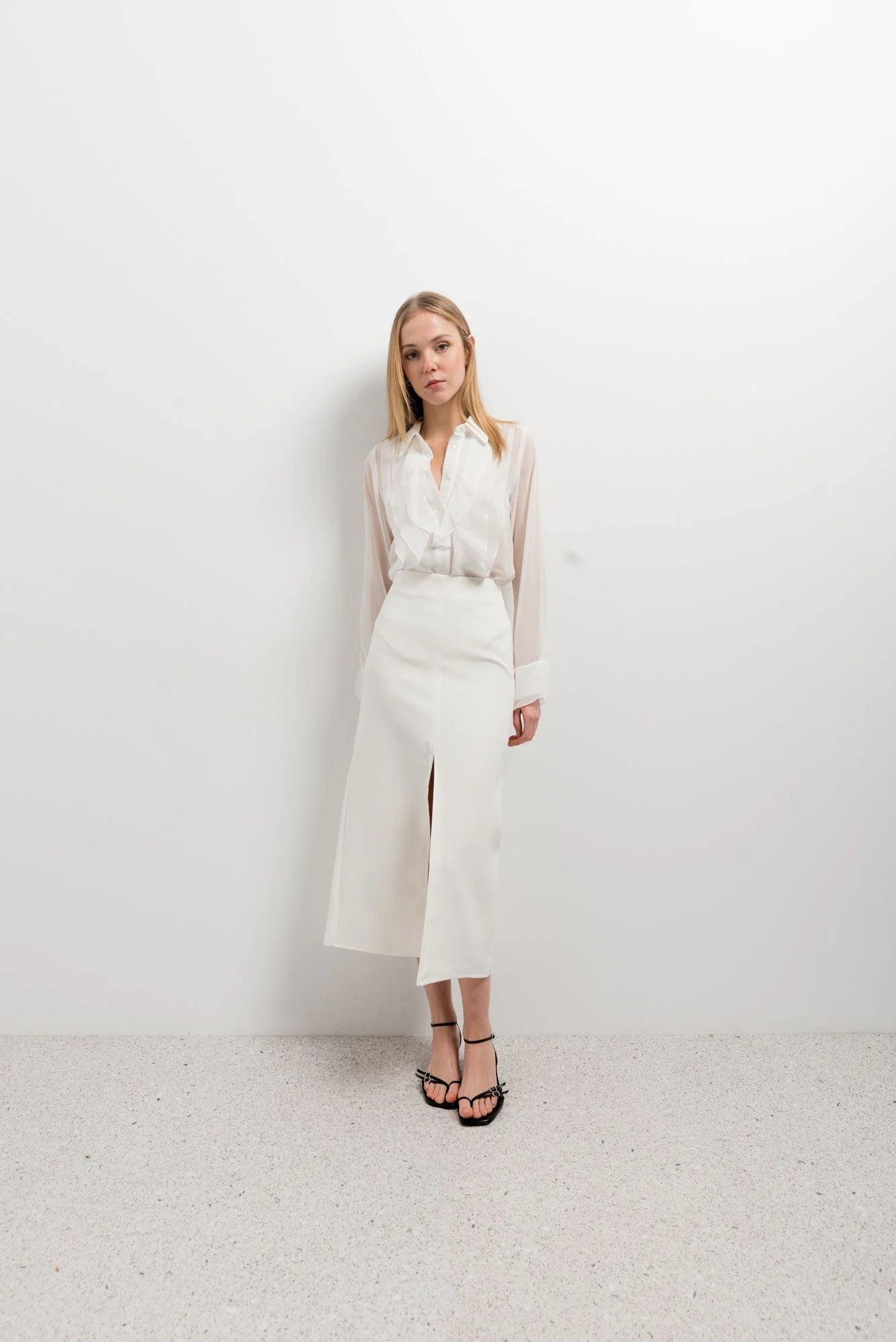 Femme posant avec élégance dans une chemise à volants blanche, chic et polyvalente, associée à une jupe pour un look moderne.