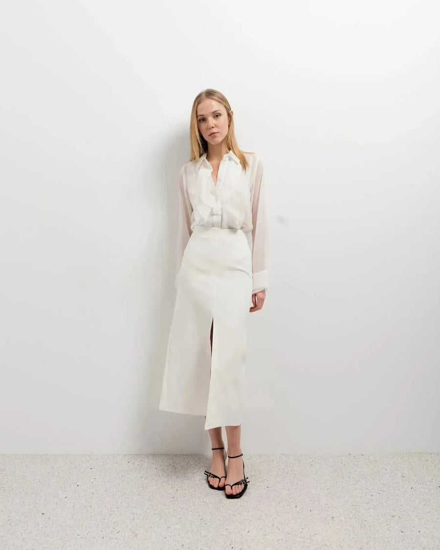 Femme posant avec élégance dans une chemise à volants blanche, chic et polyvalente, associée à une jupe pour un look moderne.