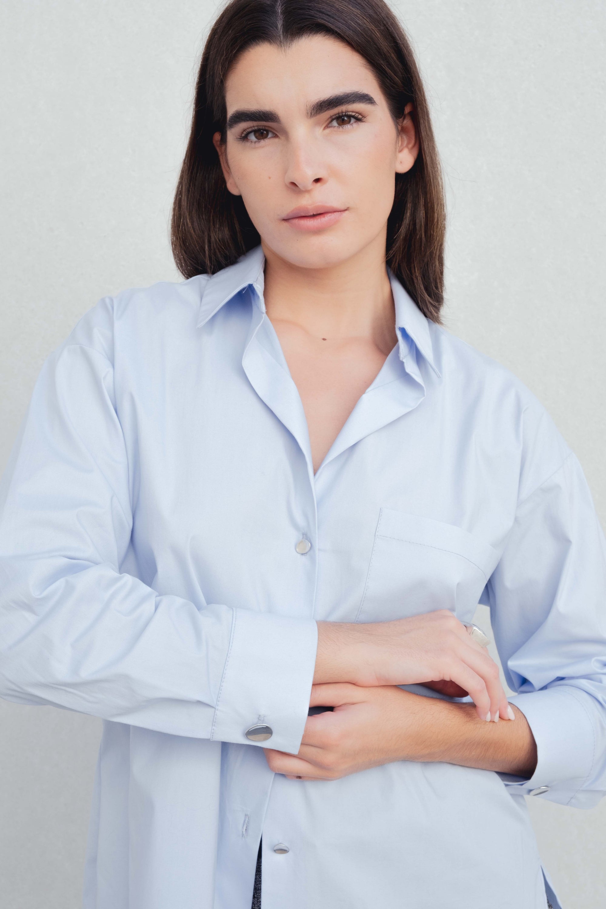 Une femme portant une chemise oversize popeline bleu ciel avec manches longues, mettant en valeur le style moderne et élégant de cette chemise oversize femme.