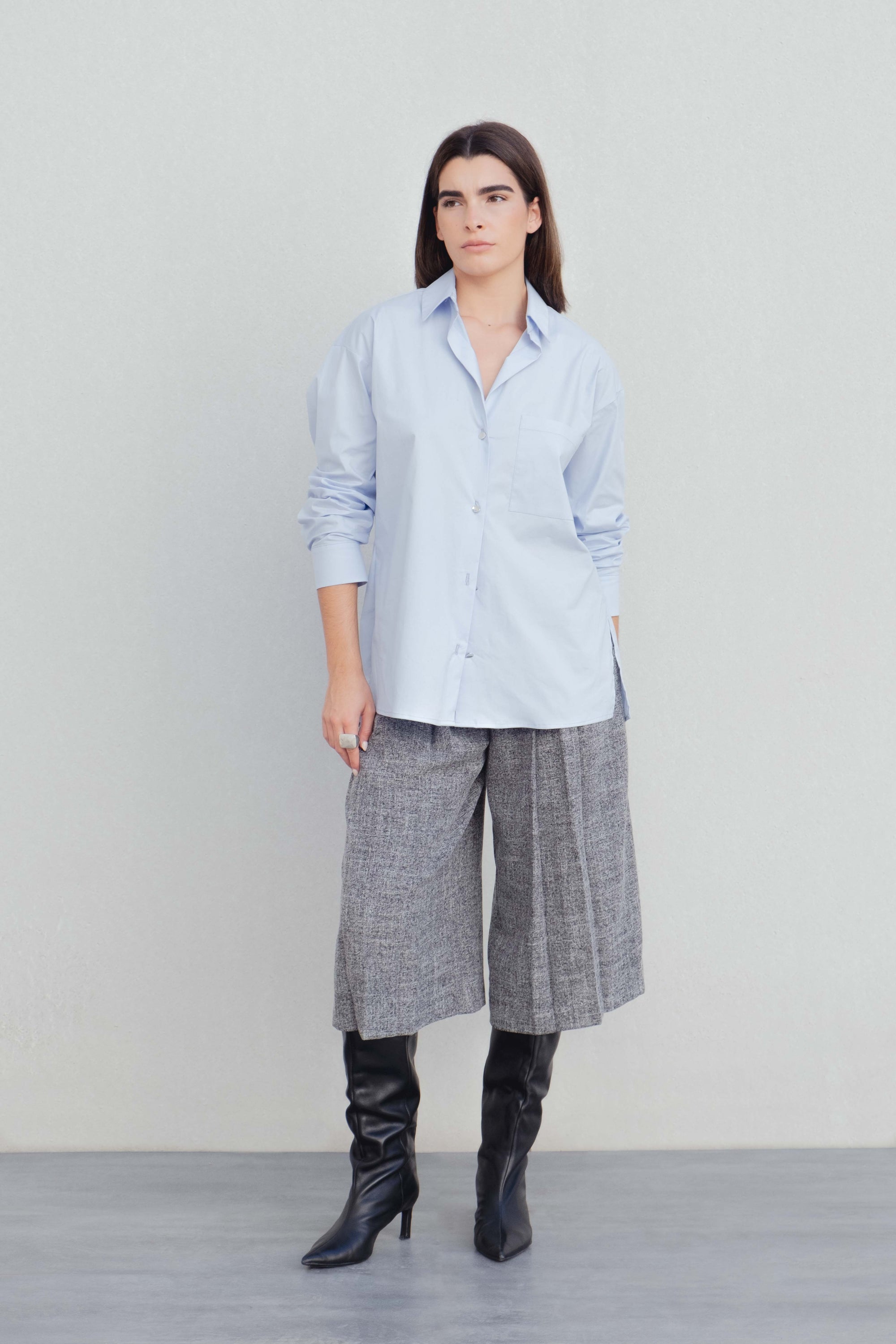 Modèle féminin affichant une chemise oversize popeline bleu ciel avec une coupe ample, associée à un pantalon à carreaux, illustrant le look décontracté de la chemise oversize femme.