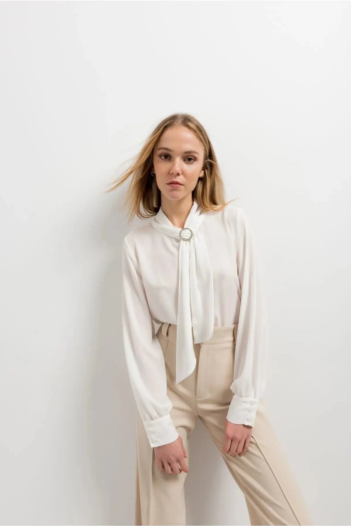 Chemisier blanc à col papillon avec manches longues, détails en argent et pantalon large beige