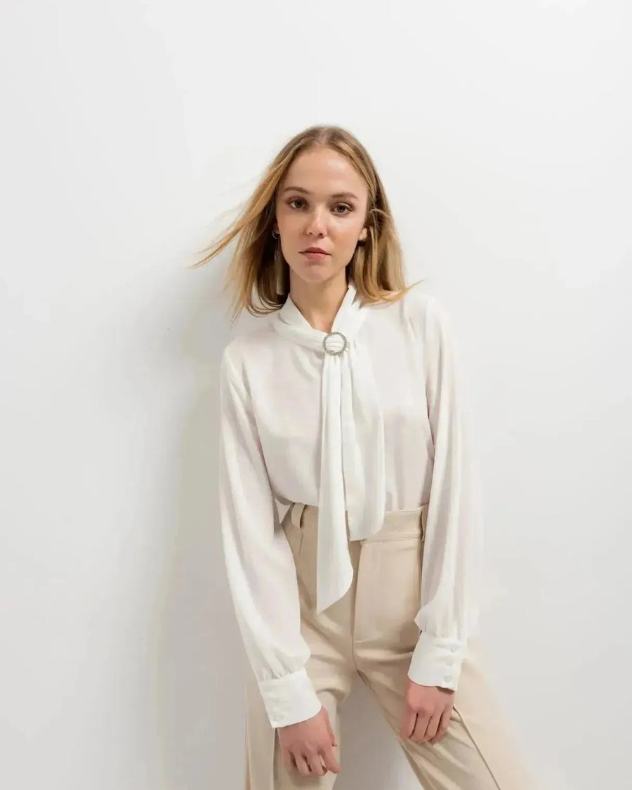 Chemisier blanc à col papillon avec manches longues, détails en argent et pantalon large beige