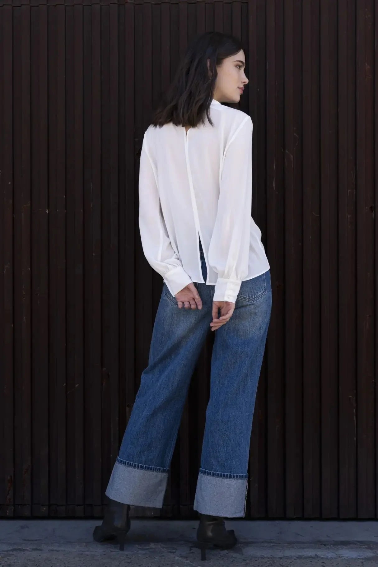 Femme portant un chemisier blanc à col papillon, jeans larges et bottes foncées