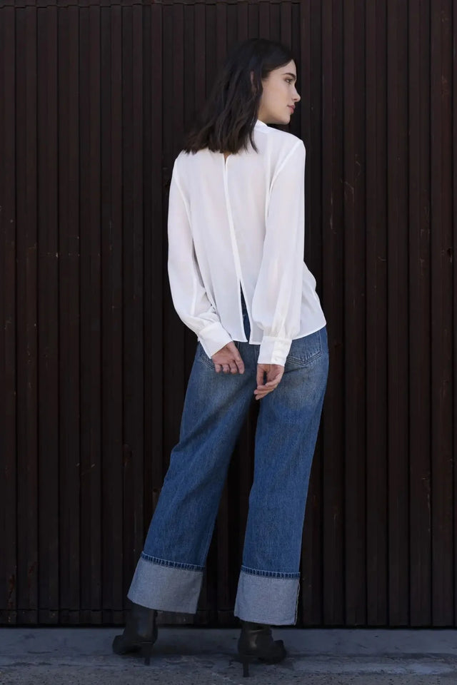 Femme portant un chemisier blanc à col papillon, jeans larges et bottes foncées