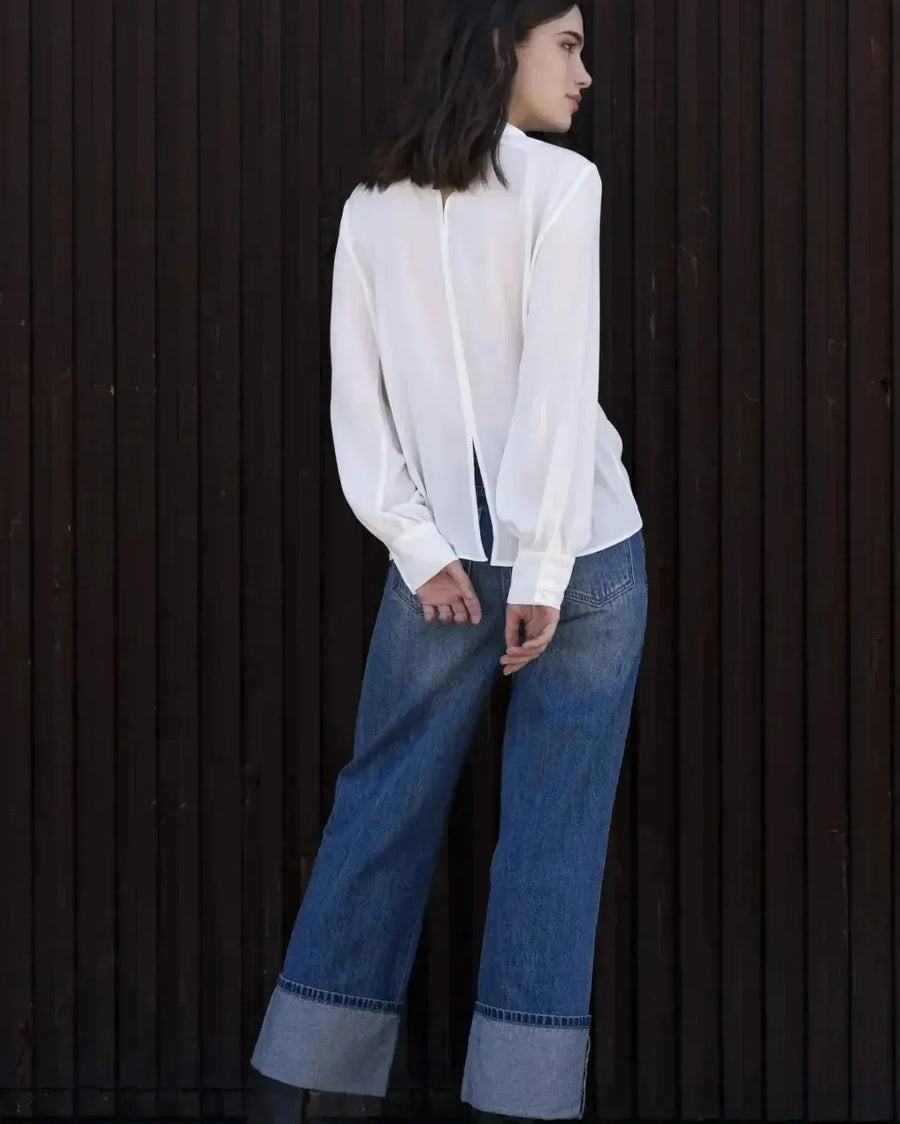 Femme portant un chemisier blanc à col papillon, jeans larges et bottes foncées
