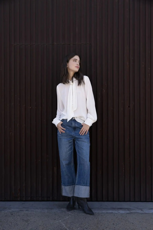 Femme portant un chemisier blanc à col papillon et jeans à jambes larges