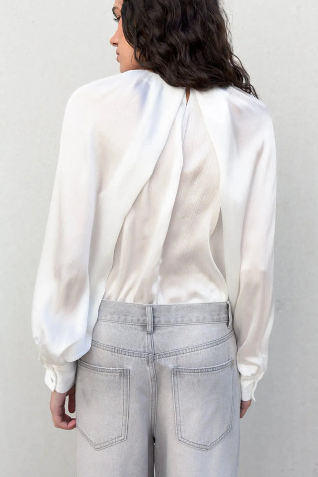 Femme de dos mettant en avant la blouse satin élégante, en exhibant son design chic et contemporain.