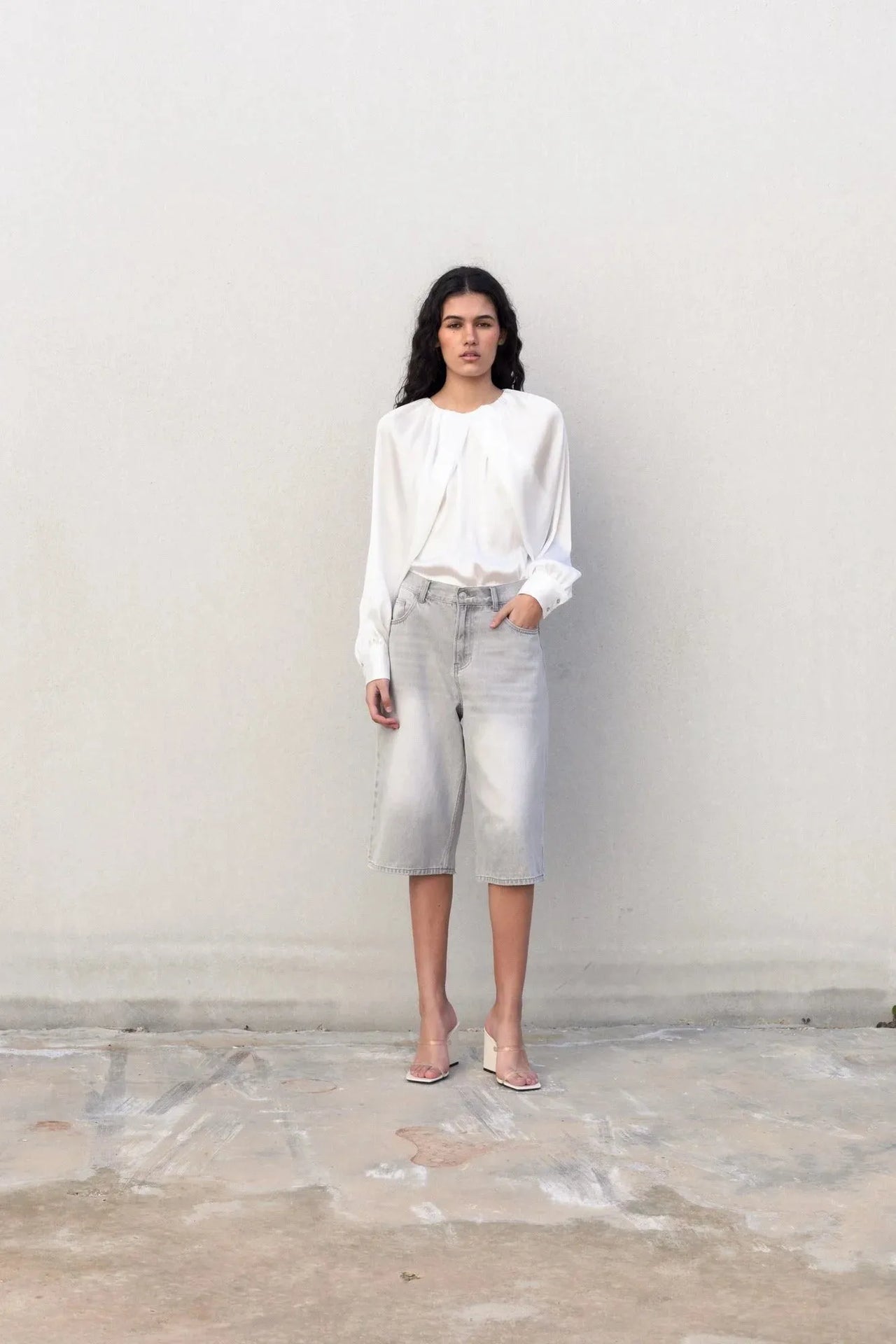 Femme se tenant debout en blouse satin élégante, capturant une ambiance chic et confortable tout en posant.