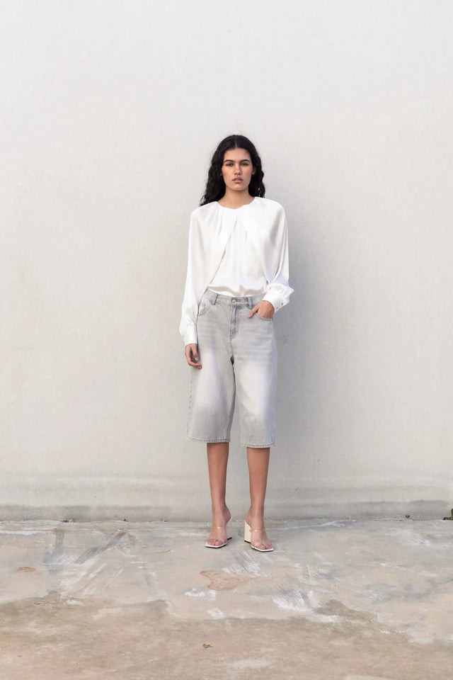 Femme se tenant debout en blouse satin élégante, capturant une ambiance chic et confortable tout en posant.