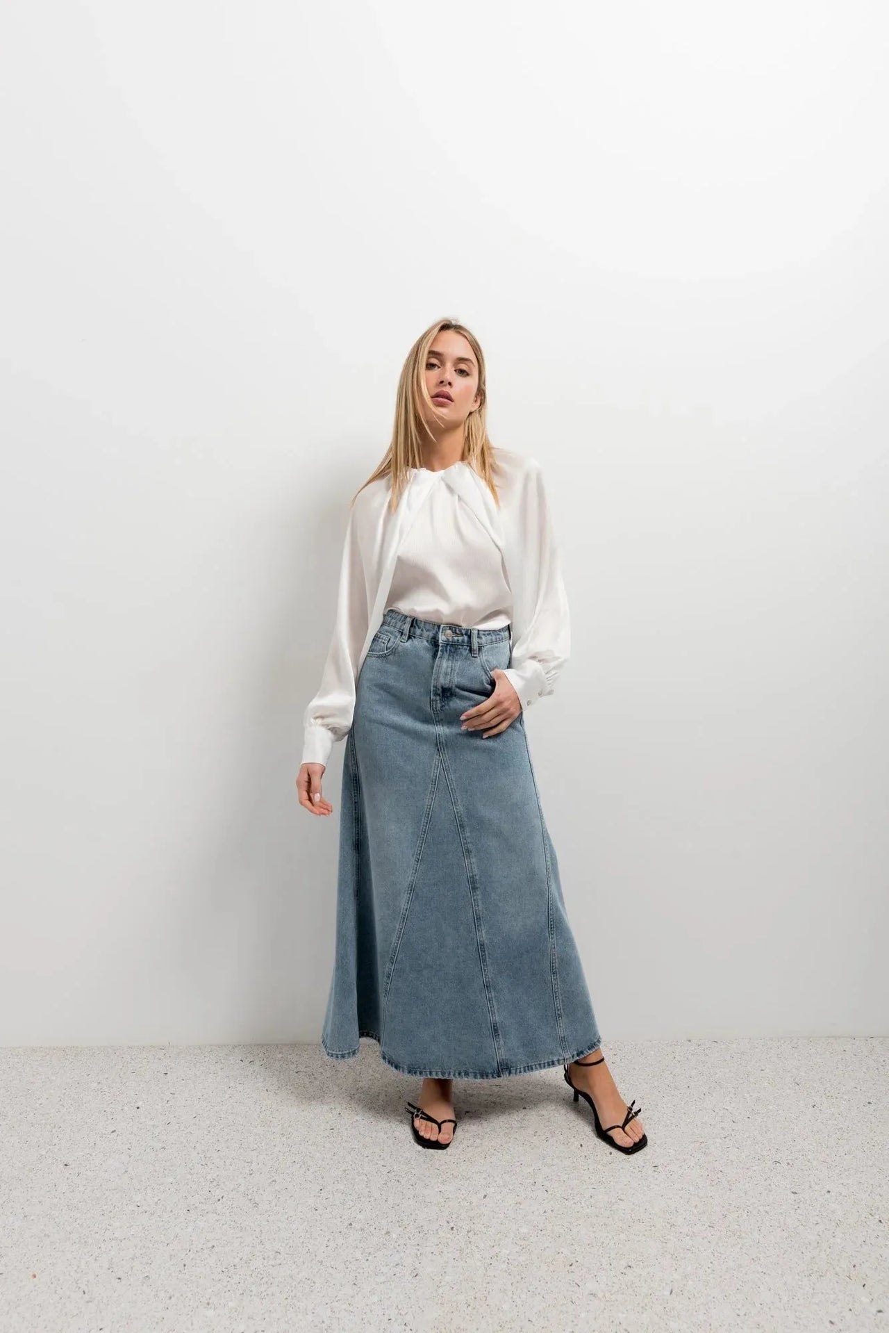 Femme posant dans une blouse satin élégante avec une jupe en denim, démontrant le style chic et polyvalent.