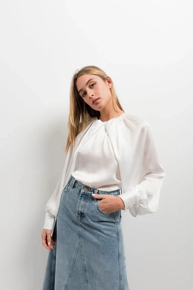 Femme en blouse satin élégante, posant décontractée avec une jupe, illustrant le style chic et confortable.